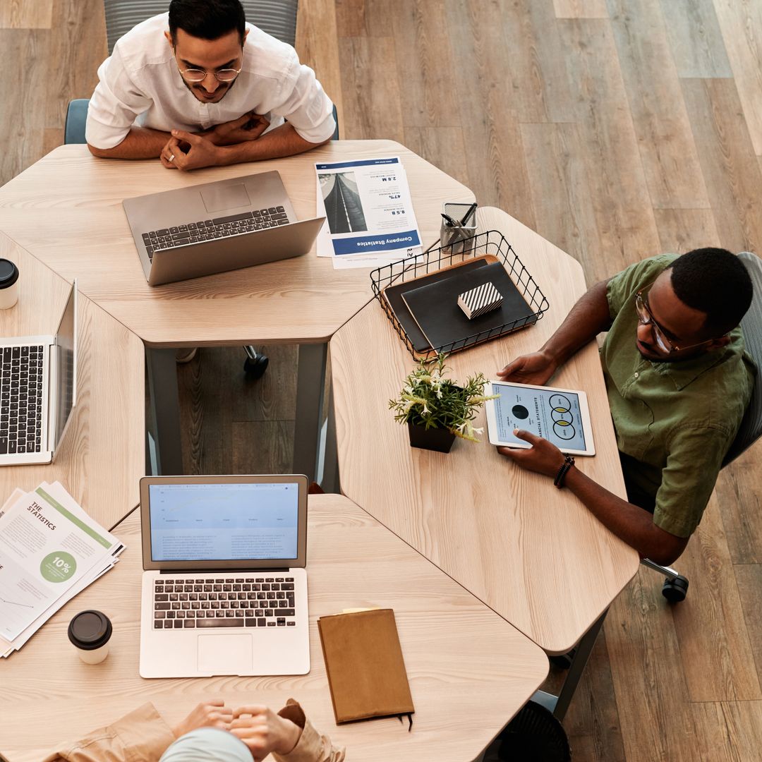 Overhead view of a diverse team discussing projects around laptops