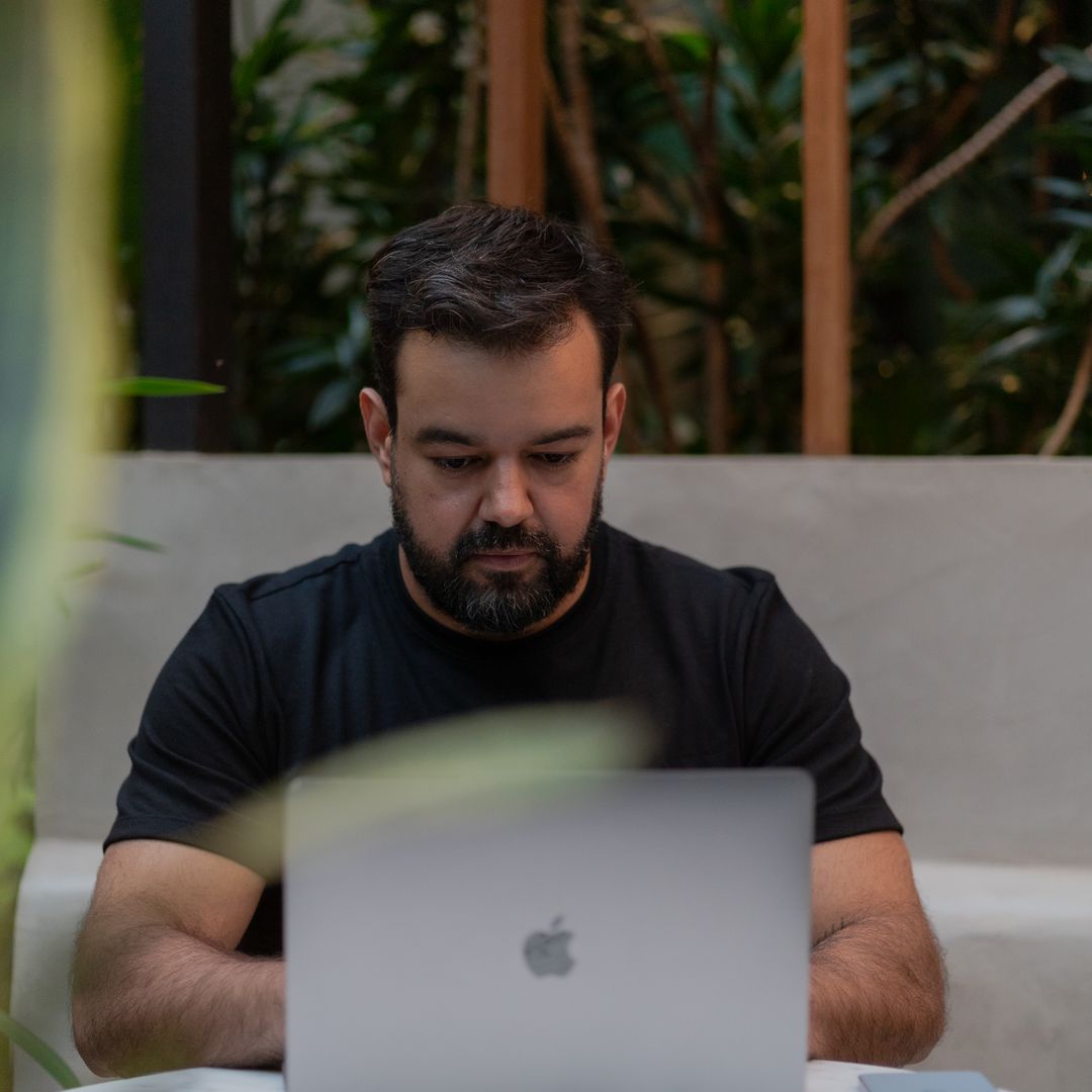 A man working on a laptop outdoors surrounded by green plants