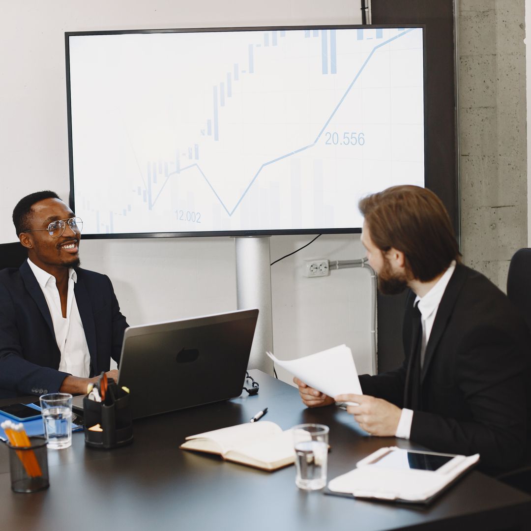 Two business owners discussing sales data on a large screen in a modern office