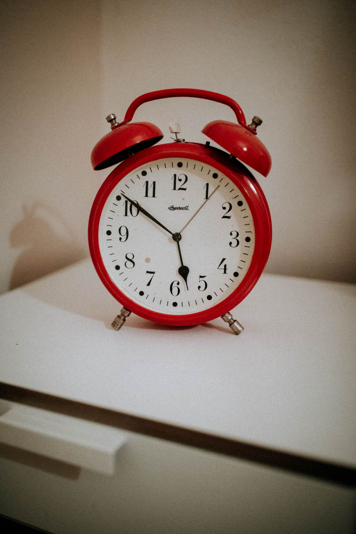A red vintage twin-bell alarm clock on a white bedside table