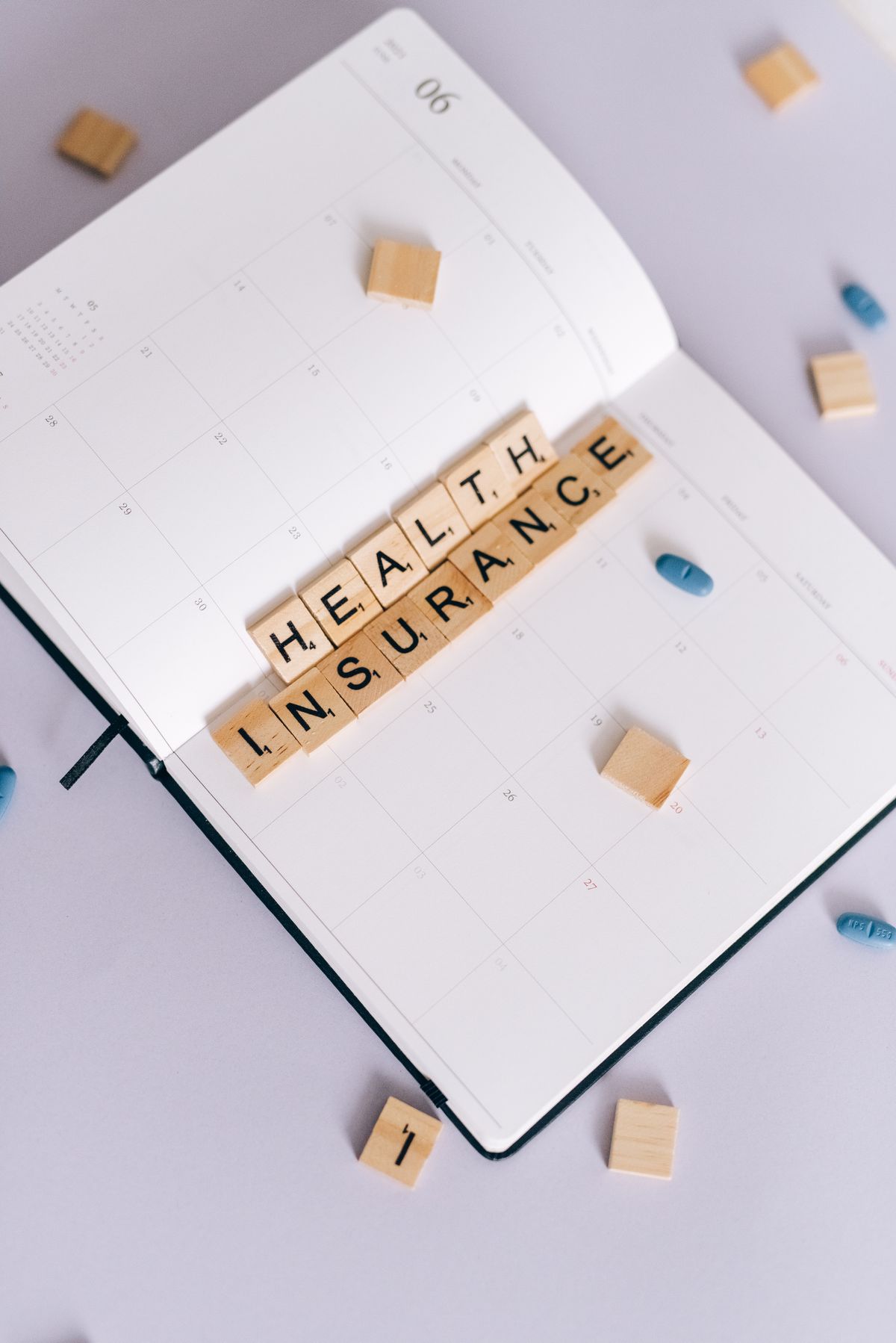 Health insurance tiles on a June calendar with pills, flat lay