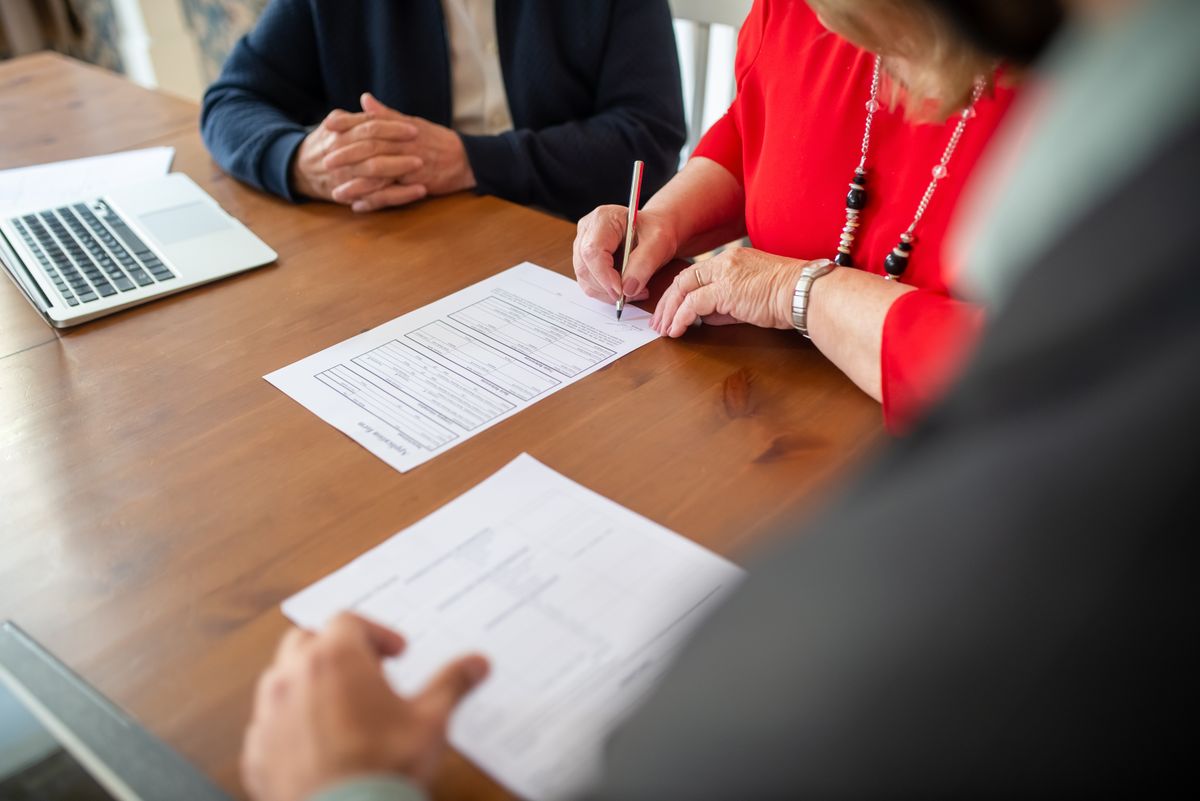 Senior couple signing insurance paperwork with an advisor at a wooden table