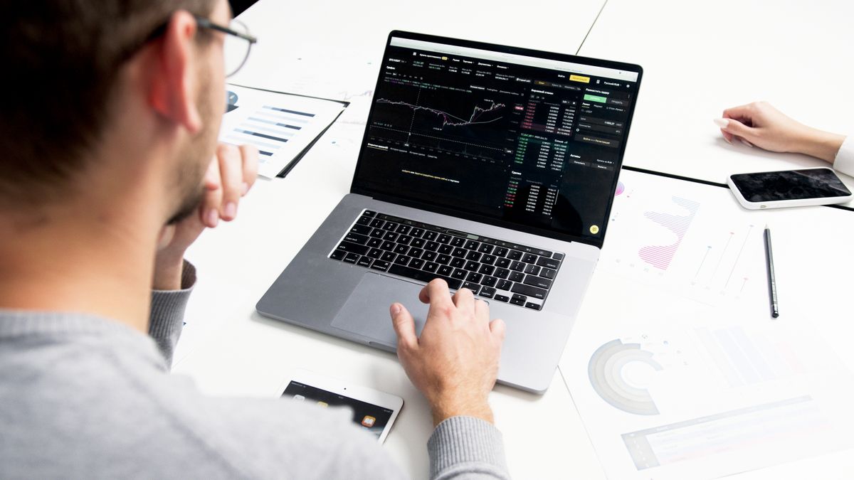 Person using a laptop showing investment charts on screen