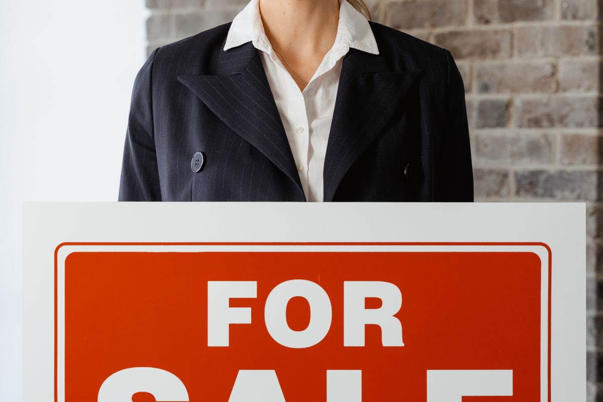 Confident woman holding a For Sale sign