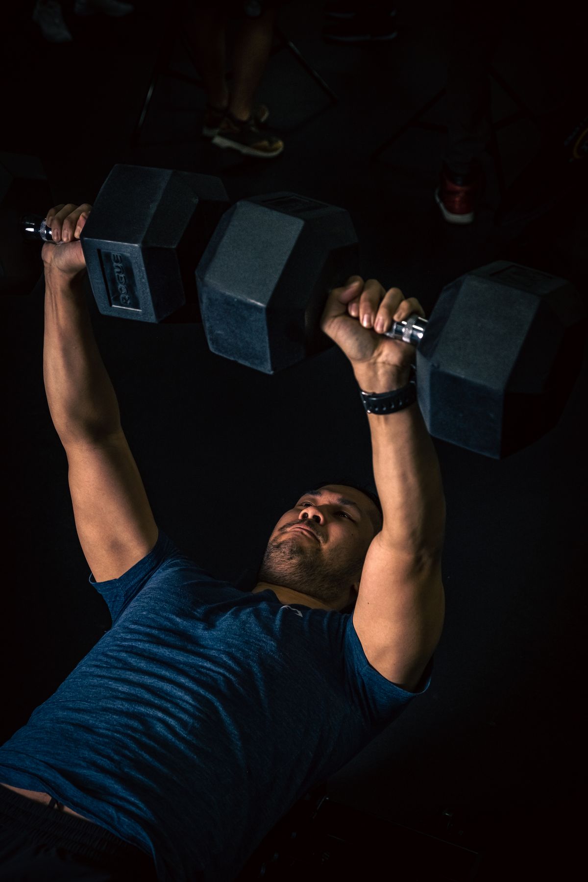 A man performing a dumbbell bench press in a dark gym