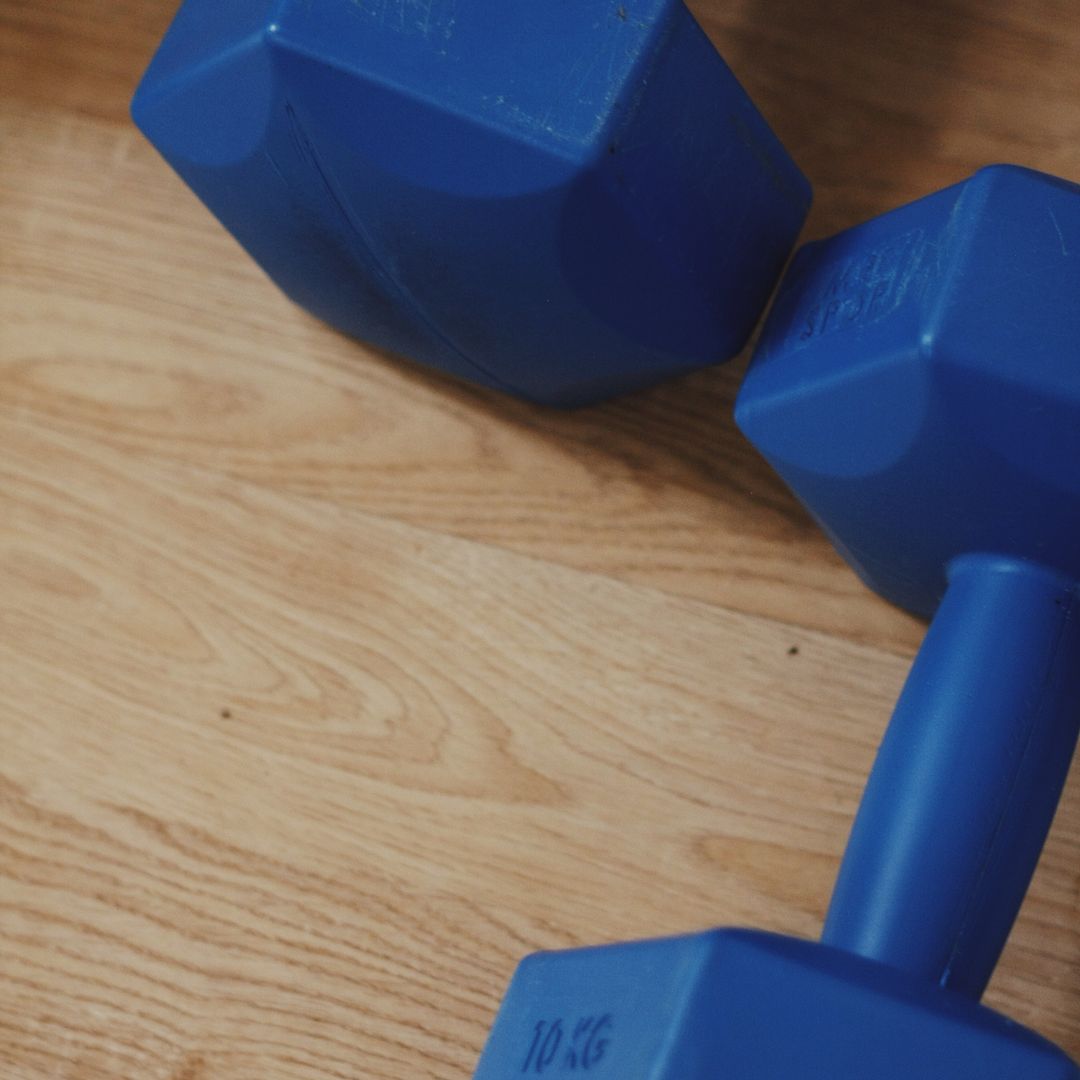 A pair of blue 10 kg dumbbells on a wooden floor at home